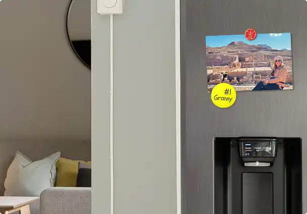 A printed Print Your Trip travel postcard displayed with magnets on a kitchen refrigerator at home